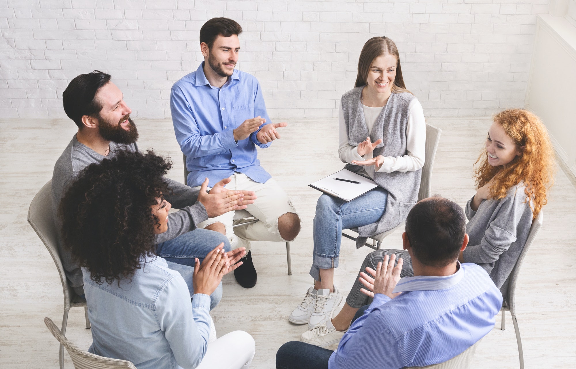 Friendly therapy group members applauding to young woman's progress in rehabilitation